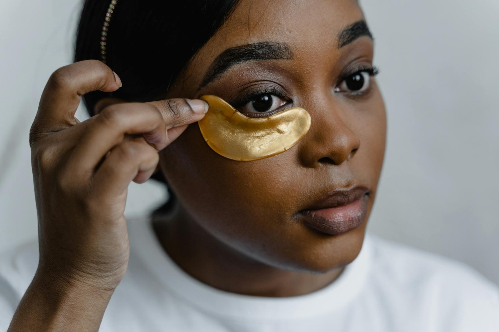 Close-up of a woman applying gold eye patches for skincare routine.
