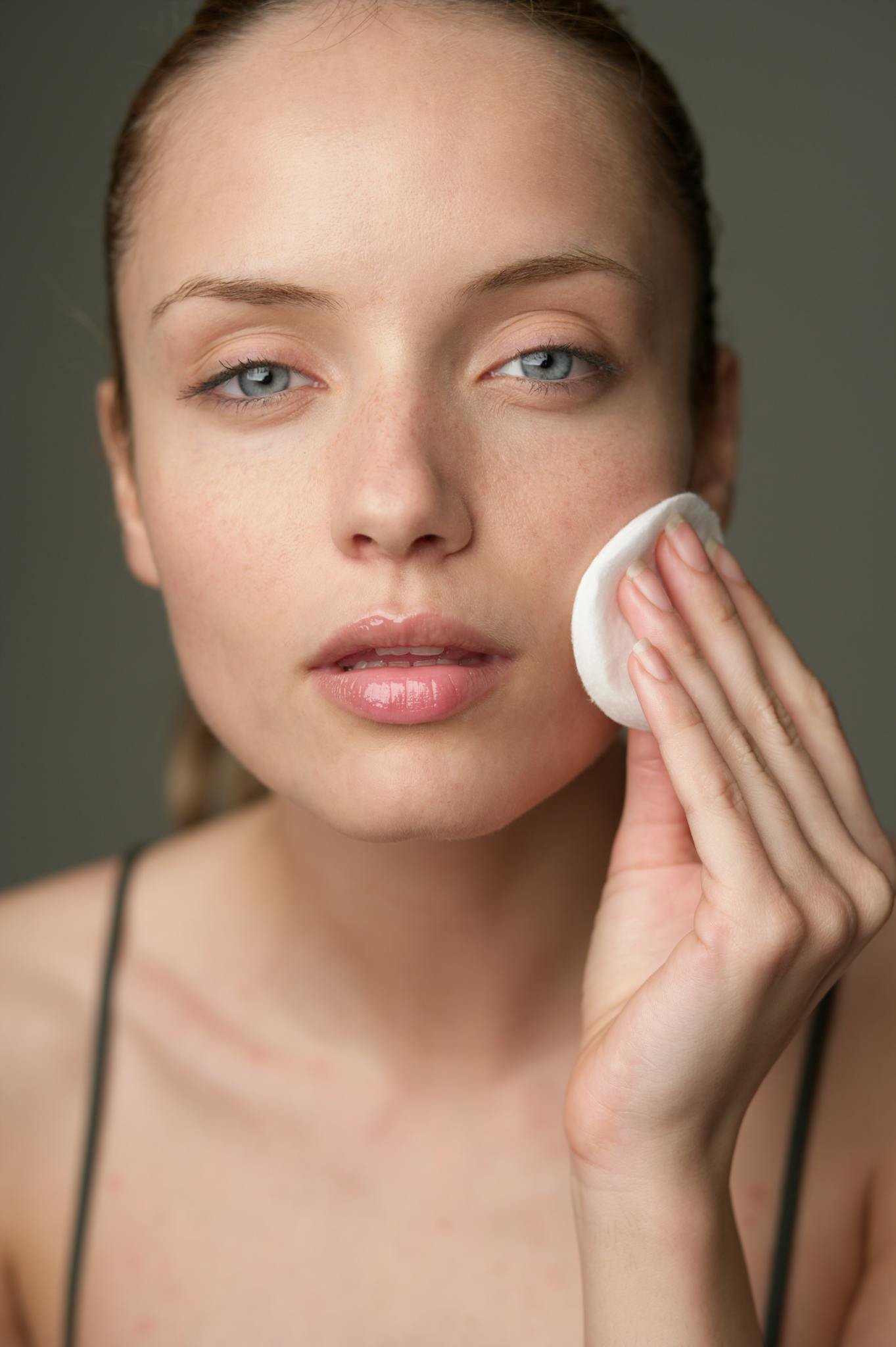Young woman using a cotton pad for skincare, highlighting beauty routine.